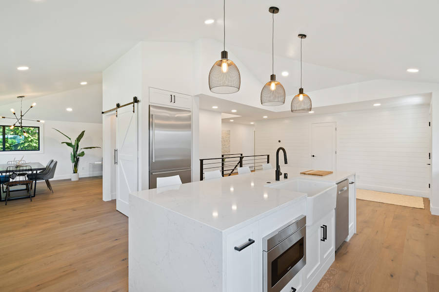 A white kitchen and dining room is well-lit by a variety of in-ceiling lighting.